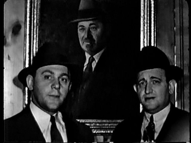 A frame from a film shot at the factory in 1940s, featuring Streitâs owners, brothers Jack Streit (1910-1998) at left and Irving Streit (1900-1982) at right, in front of a painting of their father, founder Aron Streit
